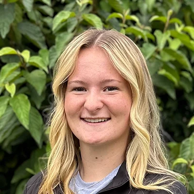 Orthodontic Assistant Allyse Smiling In Front Of A Hedge