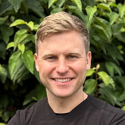 Orthodontist Daniel Wright Smiling In Front Of A Hedge