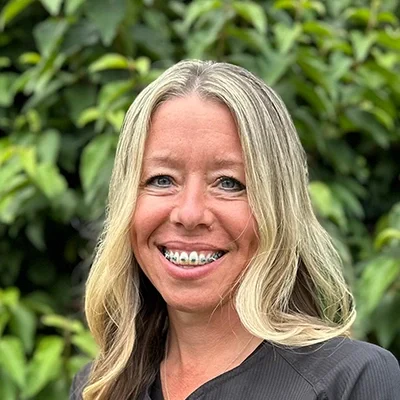Orthodontic Assistant and Lab Technician Marcey Smiling In Front Of A Hedge