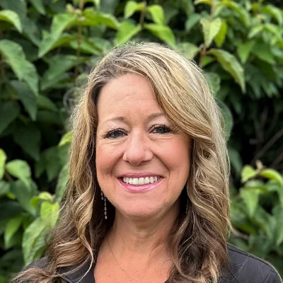 Dental Hygienist Monica Smiling In Front Of A Hedge