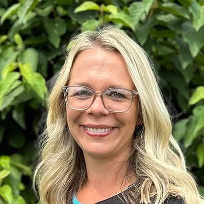 Scheduling Coordinator Daniell Smiling In Front Of A Hedge