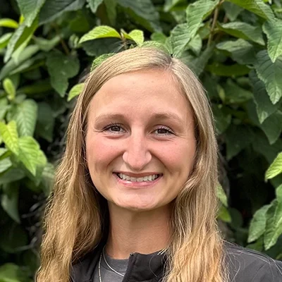 Orthodontic Assistant Rilley Smiling In Front Of A Hedge